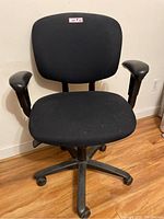 Front view of black office chair showing seat, backrest, and armrests with wear on fabric and missing plastic cover under right armrest.
