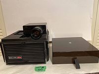 Front and side view of Bell & Howell AF 70 projector with lens and attached components, showing black body and some wear.