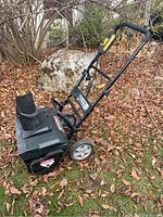 Angle side view of the Yardworks green and black electric snowblower showing wheels, chute, and handle with control button.