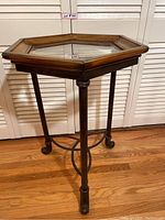 Front view of hexagonal wooden framed glass top stand with iron legs and connecting iron brace.