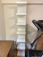 Front view of the tall narrow white IKEA shelving stand showing six staggered shelves.