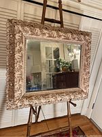Full view of vintage ornate wall mirror on an easel, showing rectangular mirror with detailed carved frame and some wear.