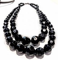 Full view of the double strand black faceted art glass bead necklace showing bead size variation and metal clasp.