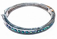 Top-down view of the vintage hinged bangle showing the silver-tone metal setting and emerald and blue rhinestones inlaid around the band.