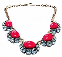 Front angled close-up of gold-tone chain necklace showing red oval cabochon stones surrounded by clear rhinestones.