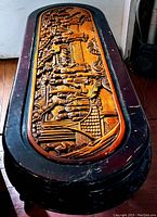 Top view of the oval coffee table showing the hand carved Asian scene on the wooden panel with figures, pagodas, and nature motifs.