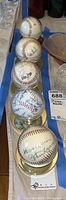 Five autographed baseballs displayed in clear cases with gold bases, showing the front signatures and arrangement of the lot.