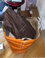 Photo showing an orange shopping bag containing a brown Vera Bradley pouch in protective cover, surrounded by other bags and items on a table.