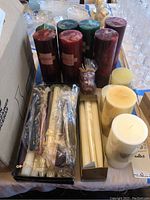 Full view of assortment of tall and pillar candles including clear-packaged taper candles and boxed candles.