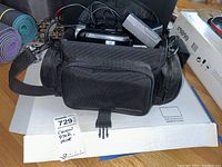 Camera bag with Canon VIXIA HF R300 camcorder, battery charger, and cables on top of the box.