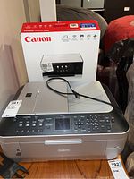 Canon PIXMA TS9020 printer with original box and power cord on top, taken from front angle.