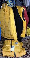 Yellow Black Dog puffer coat hanging, Polo Sport colorblock vest with red, yellow, and black hanging next to it, folded yellow Black Dog waterproof jacket on floor.