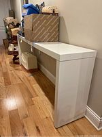 Side view of white laminate console table along wall with items on and under it.