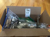 Full view of the cardboard box with numerous pieces of flatware inside plastic bags.