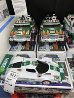 Two green Hess monster trucks with flame decals on the hood and mounted figures on roof racks, displayed on original Hess Monster Truck boxes marked 2007.