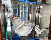 Display shelf with Lladro swan figurine, blue glass vase with metal reeds and porcelain goose figurines.
