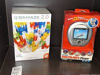 Front view of boxed Q-BA-MAZE 2.0 Big Box marble maze set and packaged Coby portable DVD/CD/MP3 player side by side.