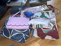 Multiple bags and purses including a pink Kate Spade purse, Black Dog canvas bags with dog illustrations, a striped strap bag, and other assorted items.