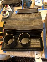 Stack of rectangular and square stoneware plates with two matching cups resting on a plate, showing texture and glaze.