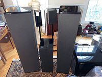Two tall floorstanding Mirage speakers with cloth grilles, one center channel speaker behind front subwoofer, two bookshelf satellites on stands.