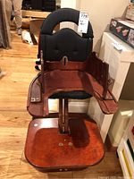 Vintage wooden high chair with black cushioned seat and backrest, showing the wooden foldable tray attached.