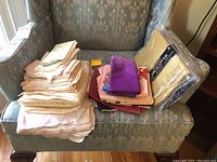 Stack of assorted cloth linens including tablecloths, napkins, placemats, mainly neutral colored fabric, several folded pieces and vibrant Japanese furoshiki cloths