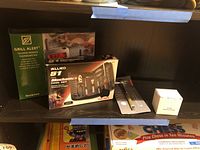 Photo shows Allied 51-piece mechanic's tool set box, Broil King Grill Alert talking remote thermometer in green box, a grill brush head package, a handy hammer tool box, all on a dark shelf.