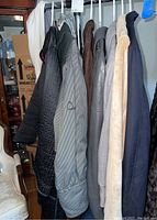 6 women's jackets and shirts hanging on rack in neutral colors including black, gray, brown, beige, blue