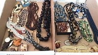 Full view of various beaded necklaces and brooches arranged in two cardboard trays, showing a range of bead styles, colors, and sizes.