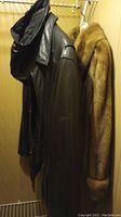 Black leather coat with removable hood and thermolite lining hanging beside brown mink fur coat.