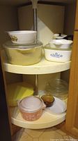 View of shelf with multiple CorningWare and Pyrex casserole and baking dishes showing patterns