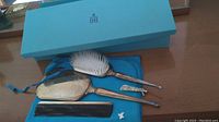 Dresser set displayed on a surface showing the blue box, blue felt wrap, hairbrush, hand mirror, and black comb.