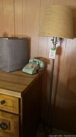 Photo showing floor lamp with beige tapered shade, blue rotary phone and wooden furniture