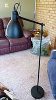 Full view of the black metal floor lamp beside a couch showing the lamp height and base.