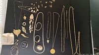Full display of assorted gold-tone necklaces, earrings, and brooches laid out on black cloth, showing variety of styles and designs.