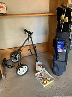 Overall lot showing canvas golf bag with clubs, Knight folding golf cart, and tray of balls, tees, and accessories