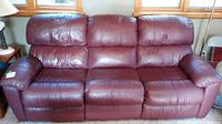 Front view of the three-seat burgundy leather sofa under windows