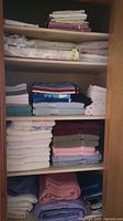 Linen closet with 5 shelves containing stacked towels, sheets, blankets in assorted colors and patterns