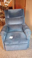 Front view of blue La-Z-Boy recliner chair with a note card on the seat showing lot number. Chair has cushioned back and arm covers matching upholstery.