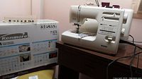 Kenmore 16774 portable sewing machine with original box and owner's manual visible, placed on a wooden surface.