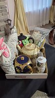 Tray holding large ceramic chicken-shaped teapot, cream and sugar set, tea cozy, scented trivet, tea diffusers, and ceramic plate.