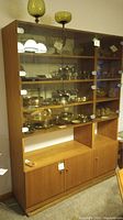 Full view of two-piece teak wall unit showing smoked glass doors, contents within shelves, and lower cabinet doors.