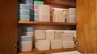 Shelf view of stacked pastel colored freezer containers, mostly white and blue with some pink and green, various sizes.