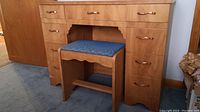 Front view of vintage blonde oak finish wood vanity with 9 drawers and matching blue upholstered bench under the knee hole.