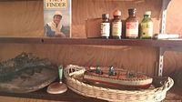 Wide shot of shelf showing the tin toy boat in a woven basket, four vintage glass bottles, and tree fungus on tray.