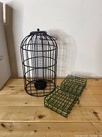 Set of three bird feeders placed on wooden surface: one black metal squirrel-proof bird feeder and two green metal suet feeders.
