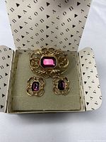 Full set of Avon brooch and earrings displayed in Avon box showing brooch and earrings with purple glass stones.