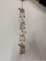 Full view of the entire hanging decoration showing four brass camels connected vertically with beads and bells.