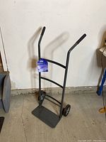 Front and side view of a black lightweight Ultra Steel hand dolly with two wheels and a flat base plate for carrying items.