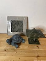 Photo of three garden accessories: boxed Nature's Path stepping stone, turtle figurine, and metal lantern with dragonfly design.